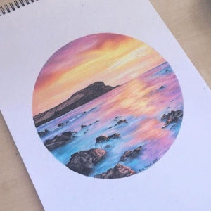 A piece of artwork by a child, featuring a colorful circular drawing of a natural landscape, displayed on a paper inside a spiral notebook.