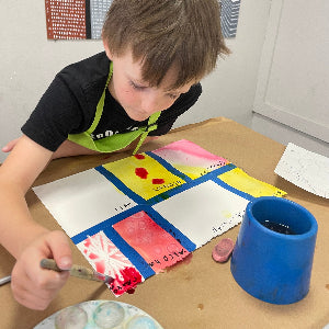Child painting a colorful abstract design on paper with a paintbrush.